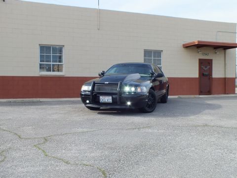2003 Ford Crown Victoria - Front three-quarter view of a black Crown Victoria with brush guard near a red door.