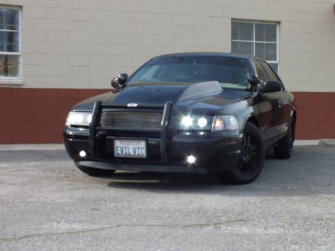2003 Ford Crown Victoria - Front three-quarter of a black Crown Victoria with brush guard and lit headlights.