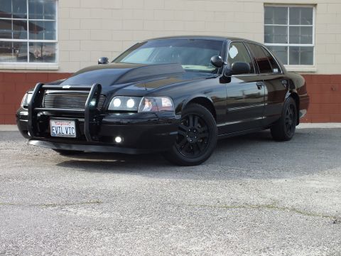 2003 Ford Crown Victoria - Black Crown Victoria with brush guard and projector lights from the front left on a lot.