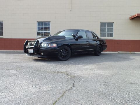 2003 Ford Crown Victoria - Front-left view of a black Crown Victoria with brush guard parked by a tan building.