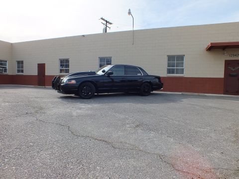 2003 Ford Crown Victoria - Distant side view of a black Ford Crown Victoria with black wheels and tinted windows beside a tan warehouse.