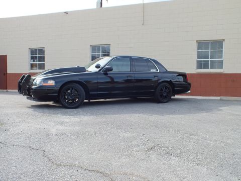 2003 Ford Crown Victoria - Black Ford Crown Victoria full side profile, grille guard up front, black alloy wheels, low stance on asphalt.