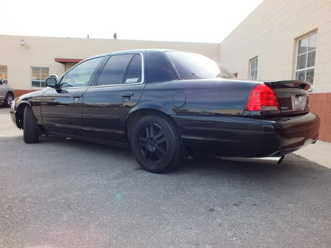 2003 Ford Crown Victoria - Rear three-quarter of a dark Crown Victoria with subtle spoiler, tinted taillights and black wheels.