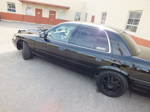 2003 Ford Crown Victoria - Side view of a black Crown Victoria sedan with black wheels; decal reading Authority on the rear glass.