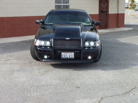 2003 Ford Crown Victoria - Head-on front view of a black Crown Victoria with hood scoop, headlights on; California plate EVIL VIC.