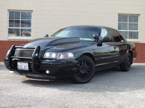 2003 Ford Crown Victoria - Front-left angle of a black Ford Crown Victoria, hood scoop and grille guard, black wheels; plate EVIL VIC.