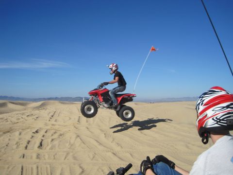 1989 Ford Bronco - A red ATV is airborne over sand dunes with a rider wearing a helmet and goggles.
