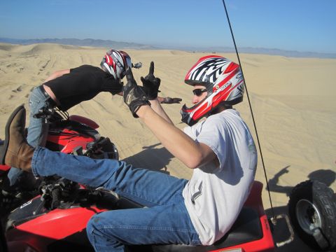 1989 Ford Bronco - Two individuals enjoy a day of riding ATVs in the sand dunes under a clear blue sky.