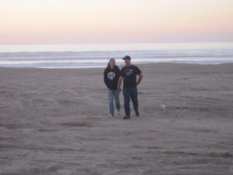 1989 Ford Bronco - A couple strolls along the shoreline as the sun sets, casting a soft glow over the ocean.