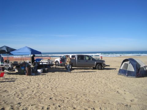1989 Ford Bronco - Two pickup trucks and tents are set up on a sandy beach with the ocean in the background.