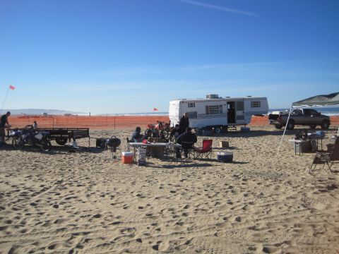 1989 Ford Bronco - A group enjoys a day at the beach with an RV, truck, and motorcycles, set against a backdrop of the ocean and a clear blue sky.