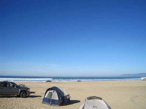 1989 Ford Bronco - A campsite is set up on the beach with tents and vehicles under a clear blue sky.