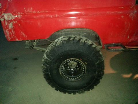 1978 Ford Bronco - Close-up of a red vehicle's rear quarter panel and a large off-road tire with a custom rim.