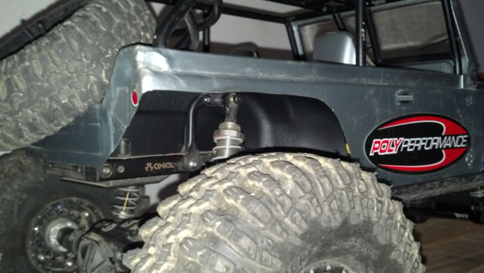 RC rock crawler rear quarter panel with 'POLY PERFORMANCE' sticker and large off-road tire