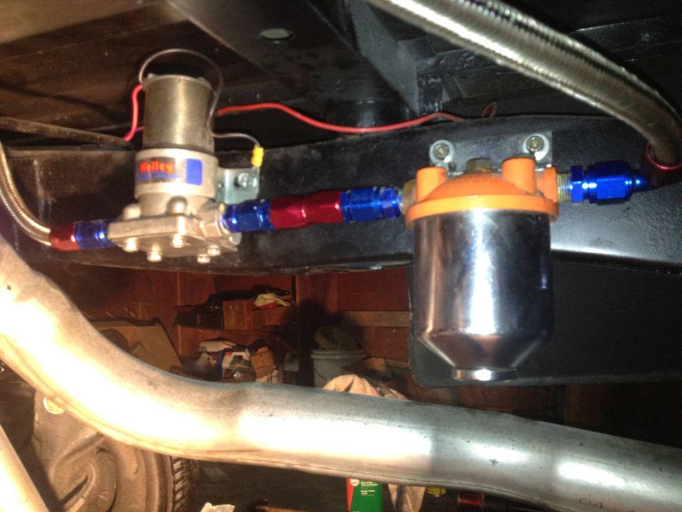 Fuel pump and chrome fuel filter assembly with red and blue fittings mounted under a vehicle