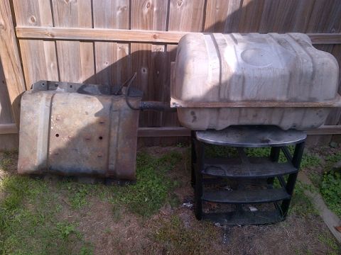 1994 Ford Bronco - Two fuel tanks, likely for a vehicle, are displayed outdoors against a wooden fence.