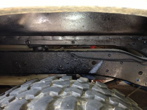 1979 Ford Bronco - Underside view of a vehicle's frame and tire, with visible undercoating and suspension components.