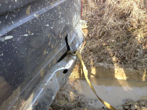 1979 Ford Bronco - A dark SUV is stuck in mud, showing damage to its rear quarter panel and a tow strap attached.