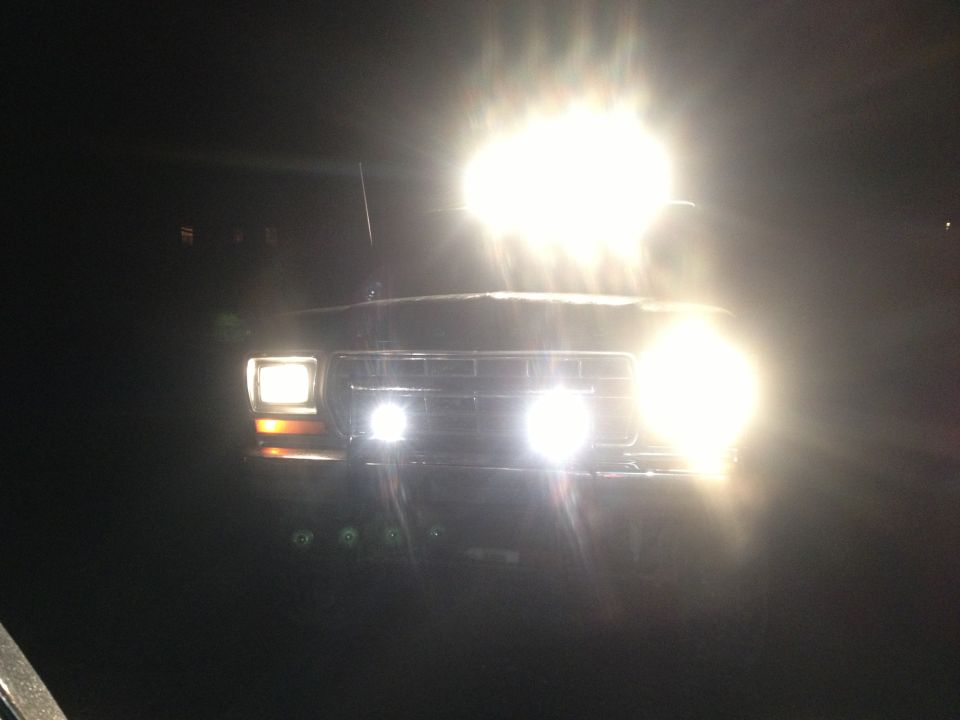 Front view of a 1978 Ford Bronco with bright headlights and auxiliary lights on at night