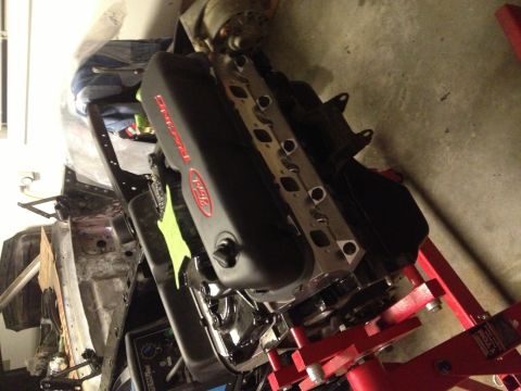 1965 Ford Mustang - Ford Racing engine on a stand, with parts of a vehicle frame in the background.