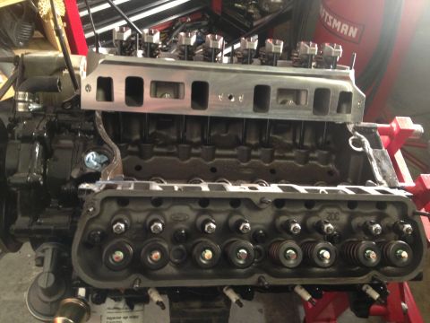1965 Ford Mustang - Close-up of an engine block assembly, showing the intake manifold and cylinder heads with valve train components.