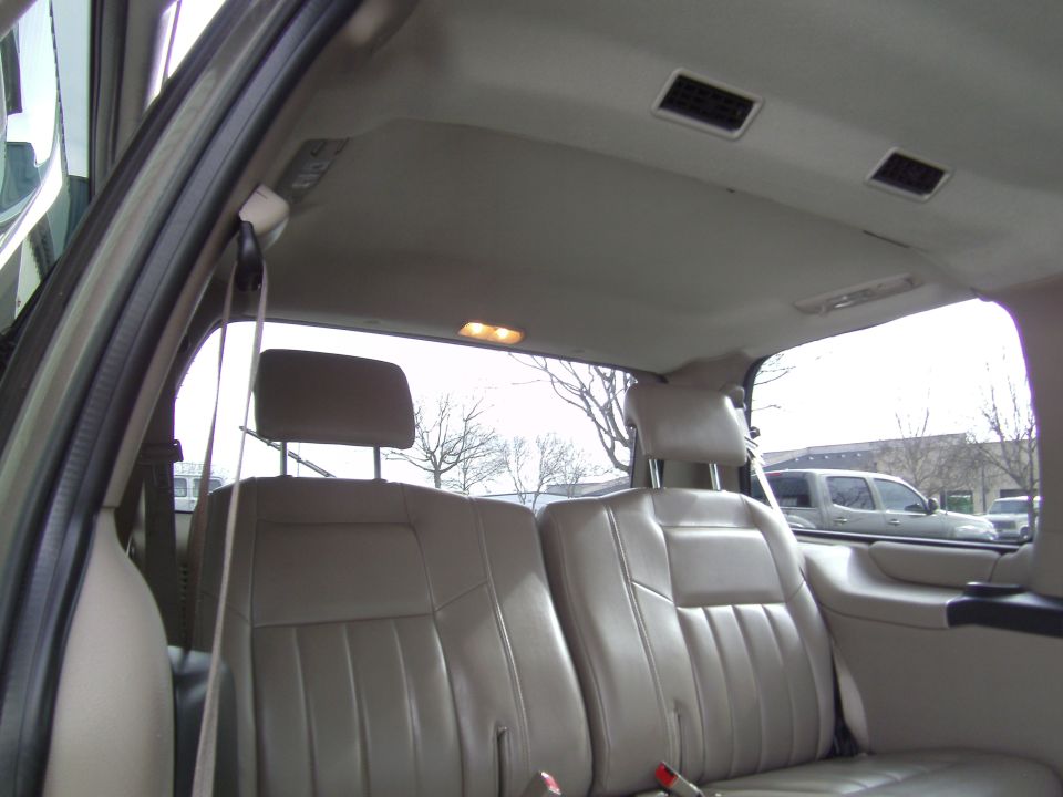 Tan minivan interior with two rows of seats visible. Air vents on ceiling