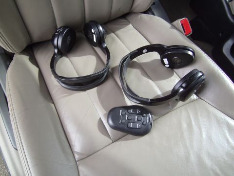 2005 Chevrolet Venture - Two headphones and a remote control rest on the tan leather seats of a vehicle.