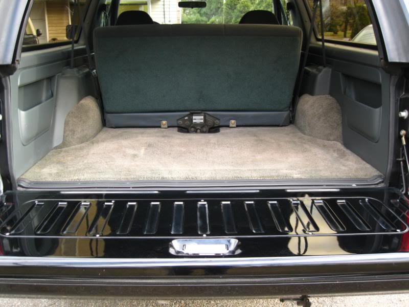 SUV rear cargo area with folded rear seat, tan and gray carpet, and open lower tailgate