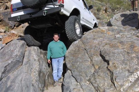 1994 Ford Bronco - A white 1992 Ford Bronco is shown off-roading on a challenging rocky terrain, with a man posing beside it.