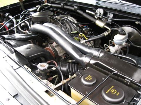 1994 Ford Bronco - Close-up view of a vehicle's engine bay, showing complex mechanical components and fluid tanks.