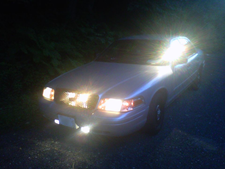 Silver Crown Victoria sedan at night with headlights and grille lights glowing, 3/4 front view