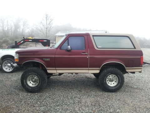 1986 Ford Bronco - A maroon Ford Bronco with a tan top is shown from the side, lifted with large tires.