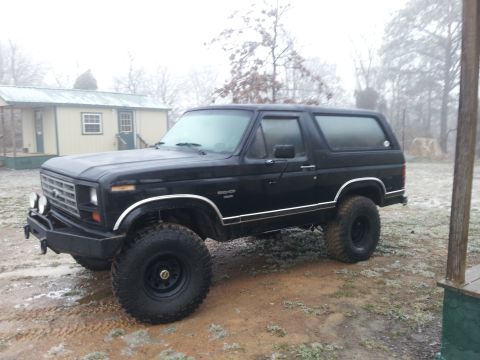 1986 Ford Bronco - This black 1986 Ford Bronco features a lifted suspension and an aftermarket front bumper, viewed from the front three-quarter angle.
