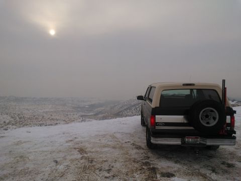 1992 Ford Bronco - A 1992 Ford Bronco is seen from the rear, parked on a snow-covered landscape under a hazy sun.