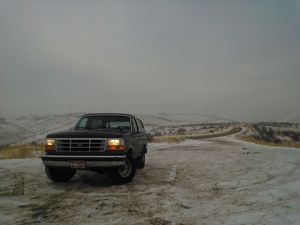 Black Ford Bronco parked on a snowy dirt road with hills in the background