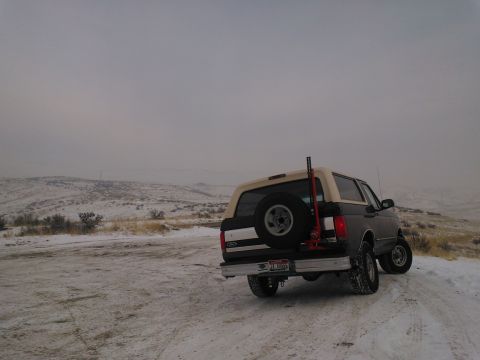 1992 Ford Bronco - A 1992 Ford Bronco is parked on a snow-covered road with hills in the background under an overcast sky.