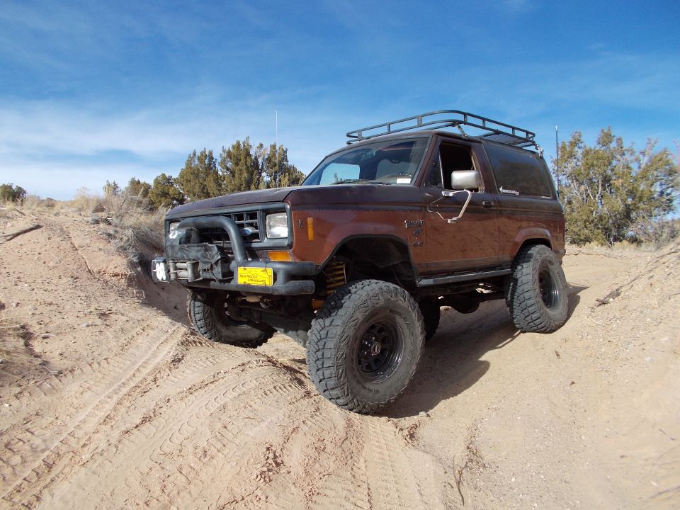 Brown Ford Bronco II with roof rack and bull bar on sandy terrain