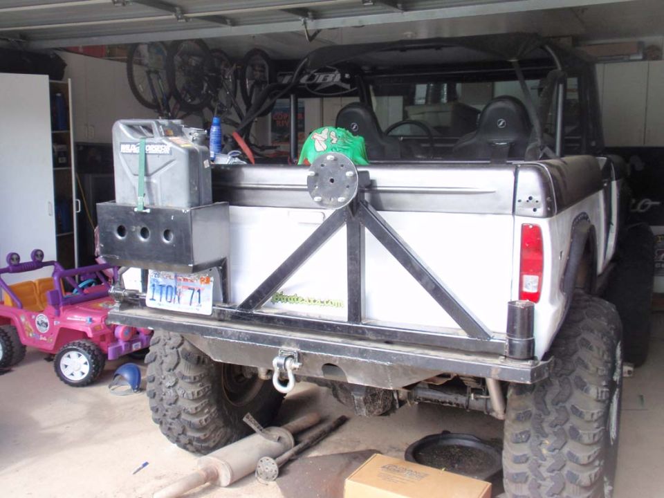 rear view of white SUV with large tires, jerry can, and spare tire mount. Pink toy Jeep nearby