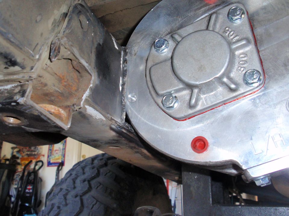 Close-up of a modified transfer case attached to vehicle frame with new welds. Tire visible below