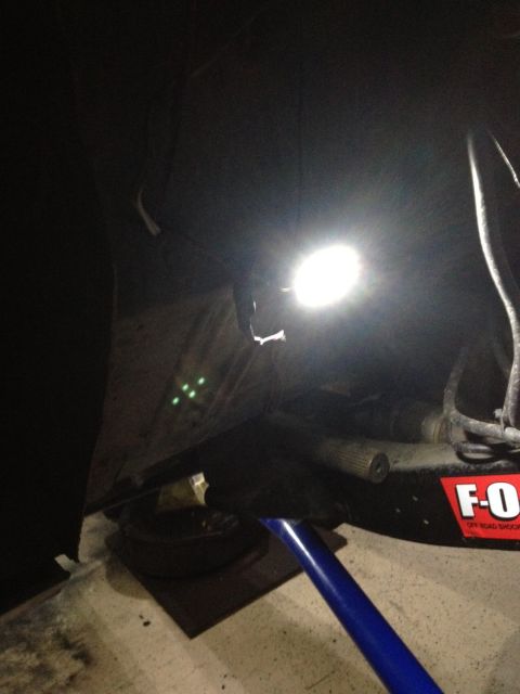 1971 Ford Bronco - A bright light illuminates the underside of a vehicle, revealing mechanical components and a red sticker.