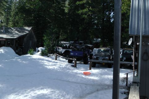 1971 Ford Bronco - Multiple off-road vehicles are parked in a snowy area next to a rustic wooden structure.