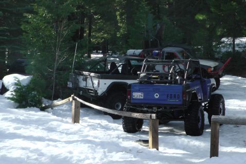 1971 Ford Bronco - Two modified off-road vehicles are parked in a snowy area with trees surrounding them.