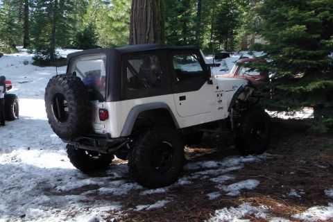 1971 Ford Bronco - A white Jeep Wrangler with a black soft top and large off-road tires is parked in a snowy, wooded area, outdoor setting.