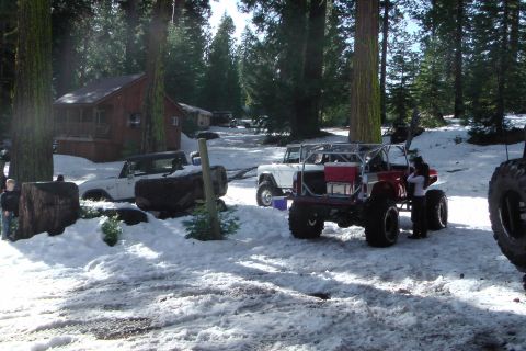 1971 Ford Bronco - Several off-road vehicles are parked in a snowy wooded area next to a cabin.