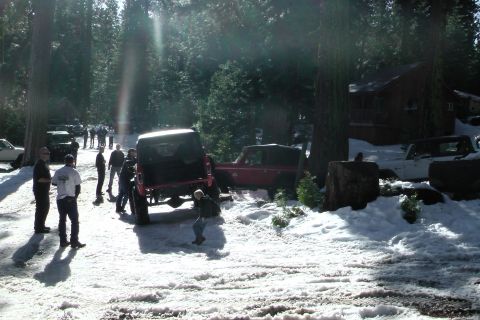 1971 Ford Bronco - People gather around vehicles in a snowy, wooded landscape with a cabin in the background.