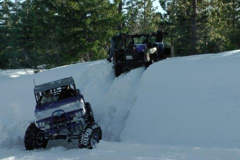1971 Ford Bronco - Off-road vehicles navigate a snowy trail, kicking up snow as they go.