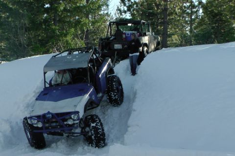 1971 Ford Bronco - Two off-road vehicles navigate a snowy incline with trees in the background.