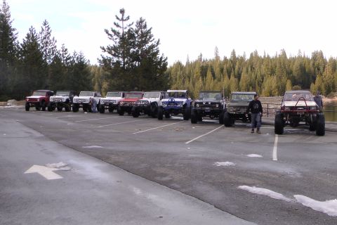 1971 Ford Bronco - Multiple off-road SUVs are parked in a lot near a wooded area and a body of water.