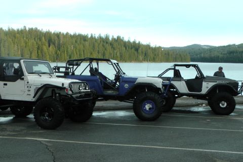 1971 Ford Bronco - Three custom off-road vehicles are parked side-by-side near a lake.