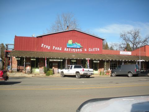 1971 Ford Bronco - A white pickup truck is parked in front of the Frog Pond Antiques & Gifts store on a sunny day.